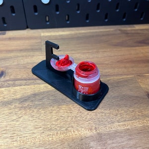 May include: A 3D printed paint pot holder with a red paint pot and a clear lid. The holder has a small, clear, removable cup for holding paint.