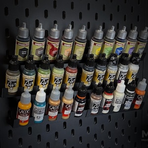 May include: A selection of paint bottles in different colours, arranged on a black pegboard. The bottles are labelled with brands such as "Speed Paint", "Model Air", and "GAC". The image includes the text "MK2 Modular Range".