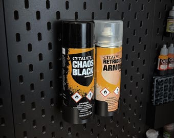 以下が含まれることがあります： シタデルブランドのロゴと「Chaos Black」と「Retributor Armour」の文字が書かれた、黒とオレンジの2本のスプレー缶。