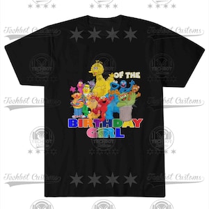 May include: Black t-shirt featuring a colorful graphic of Sesame Street characters, including Big Bird, Elmo, and Cookie Monster. The text "BIRTHDAY GIRL" is displayed in rainbow colors. The shirt has a crew neck and short sleeves.