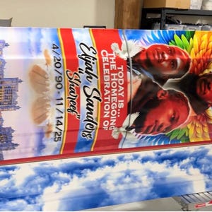 May include: A colorful casket with a vibrant design. The top features portraits of three people with angel wings, set against a sky and cloud background. Text includes "Today is... The Homegoing Celebration of Elijah Sanders 'Shareef' 4/20/90-11/14/25".