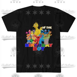 May include: Black t-shirt featuring a colorful graphic of Sesame Street characters, including Big Bird, Elmo, and Cookie Monster. The text "BIRTHDAY BOY" is displayed in vibrant, multi-colored letters. The shirt has a crew neck.