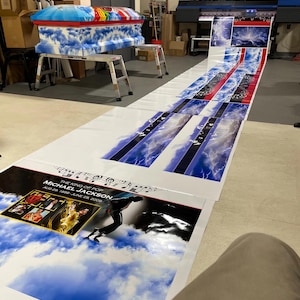 May include: A casket with a blue sky and cloud design, with a rainbow-colored top. The image also shows a large print with the text "THE KING OF POP MICHAEL JACKSON AUG 29, 1958 - JUNE 25, 2009" and images of Michael Jackson.