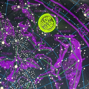 May include: Black t-shirt with a constellation map printed on it. The constellations are outlined in purple and the stars are white. The shirt has a glow-in-the-dark label that says "Glow in the Dark" with "Liquid Blue" printed below it.
