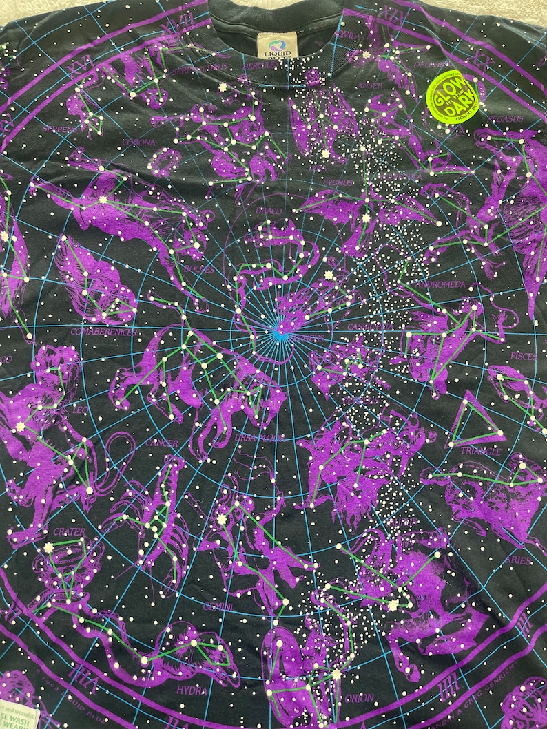 May include: Black t-shirt with a glow-in-the-dark print of a constellation map. The constellations are outlined in purple and the stars are white. The text "Glow in the Dark" is printed on a yellow tag.