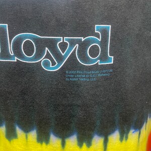 May include: Black t-shirt with a tie-dye pattern in shades of yellow, orange, red, blue, and green. The shirt features a white graphic of a triangle with the word "Floyd" printed in blue and white letters.