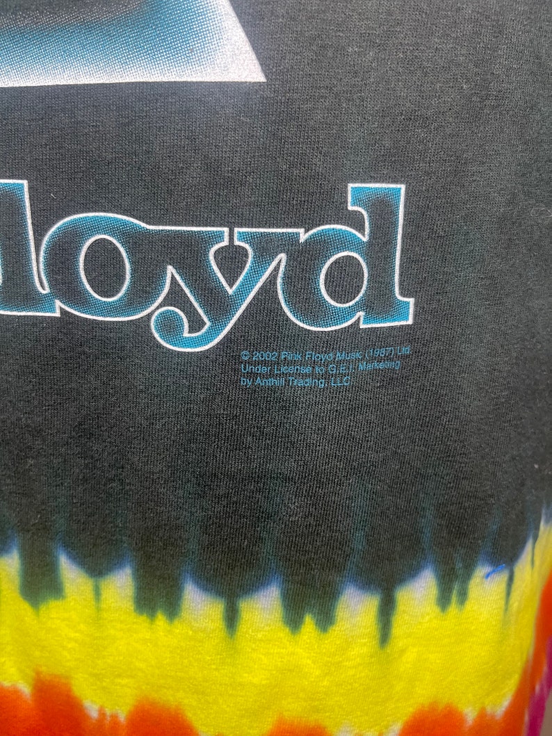 May include: Black t-shirt with a tie-dye pattern in shades of yellow, orange, red, blue, and green. The shirt features a white graphic of a triangle with the word "Floyd" printed in blue and white letters.