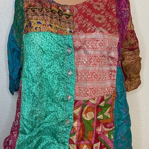 Könnte beinhalten: Eine mehrfarbige Patchwork-Seidenbluse mit Knopfleiste. Die Bluse zeigt verschiedene florale und geometrische Muster in Blautönen, Grün, Rot, Rosa und Gold.