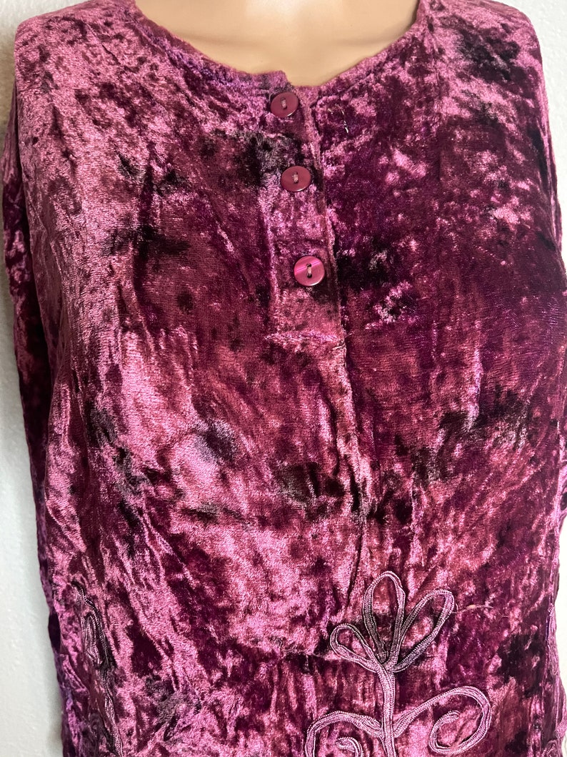 May include: A sleeveless, purple velvet top with a button-up front and a floral design embroidered on the bottom.