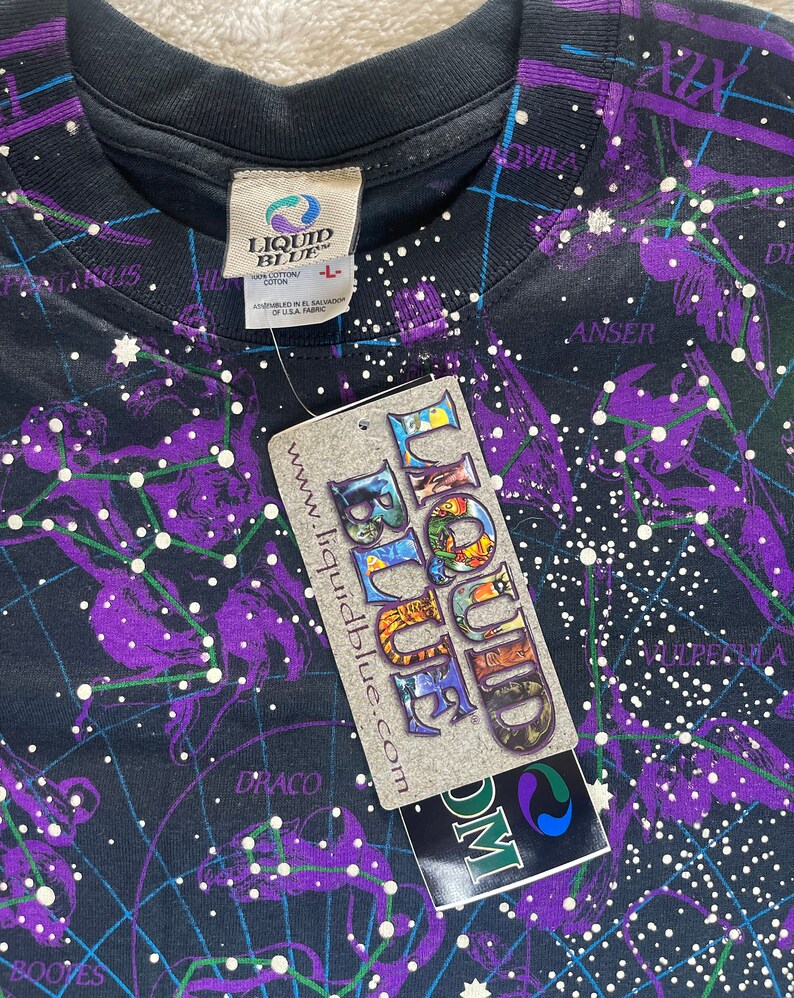 May include: A black t-shirt with a constellation print. The shirt features a purple and white design with the text "Liquid Blue" and "www.liquidblue.com".