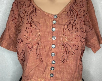 May include: A brown cropped top with short sleeves and a button-up front. The top has a floral design embroidered in red and gold thread.