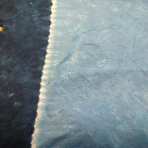 May include: A tie-dye t-shirt with a split design. One side is a deep navy blue, and the other is a lighter, sky blue. A white, vertical line separates the two colours. The fabric appears soft and slightly textured.