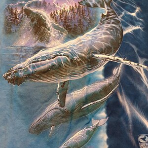 May include: Blue t-shirt with a detailed illustration of humpback whales in the ocean. The design includes whales breaching the water, with a forest and lightning in the background. The shirt has a Liquid Blue &copy;2006 logo.