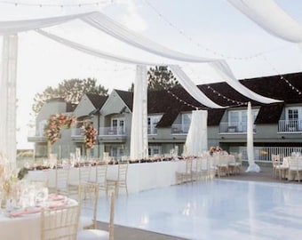May include: A white dance floor with white chairs and tables set up for a wedding reception. The dance floor is under a white canopy with white string lights.