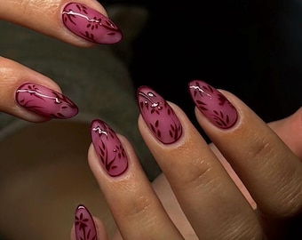 Puede incluir: Primer plano de uñas manicuradas con color burdeos y diseño floral. Las uñas son de forma ovalada y presentan un contorno burdeos oscuro con un relleno burdeos más claro. El diseño floral es de color burdeos oscuro.