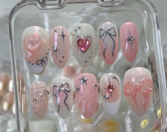 May include: A set of ten pink and white press-on nails with silver glitter, bows, stars, and rhinestones.