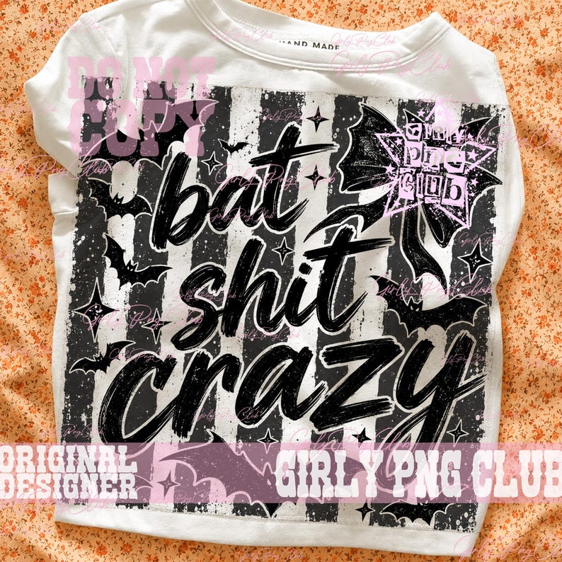 May include: A white t-shirt featuring a black and white vertical striped graphic with the text "bat shit crazy" in a bold, brush-style font. The design includes black bat silhouettes, small four-pointed stars, and a large bow with a star pattern.