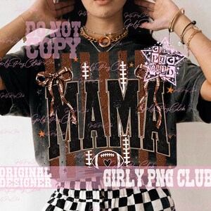 May include: A black mineral-washed t-shirt featuring the word MAMA in large black block letters with a brown football texture background. The design includes two brown football-patterned bows, white football laces, and a football graphic.