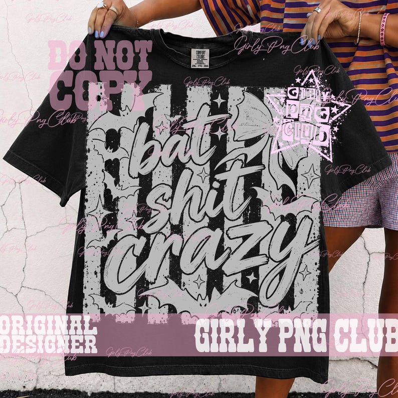 May include: A black t-shirt featuring a large graphic print with vertical stripes, scattered bat silhouettes, and star shapes. The text "bat shit crazy" is printed in a large, stylized, light-colored font across the center of the design.