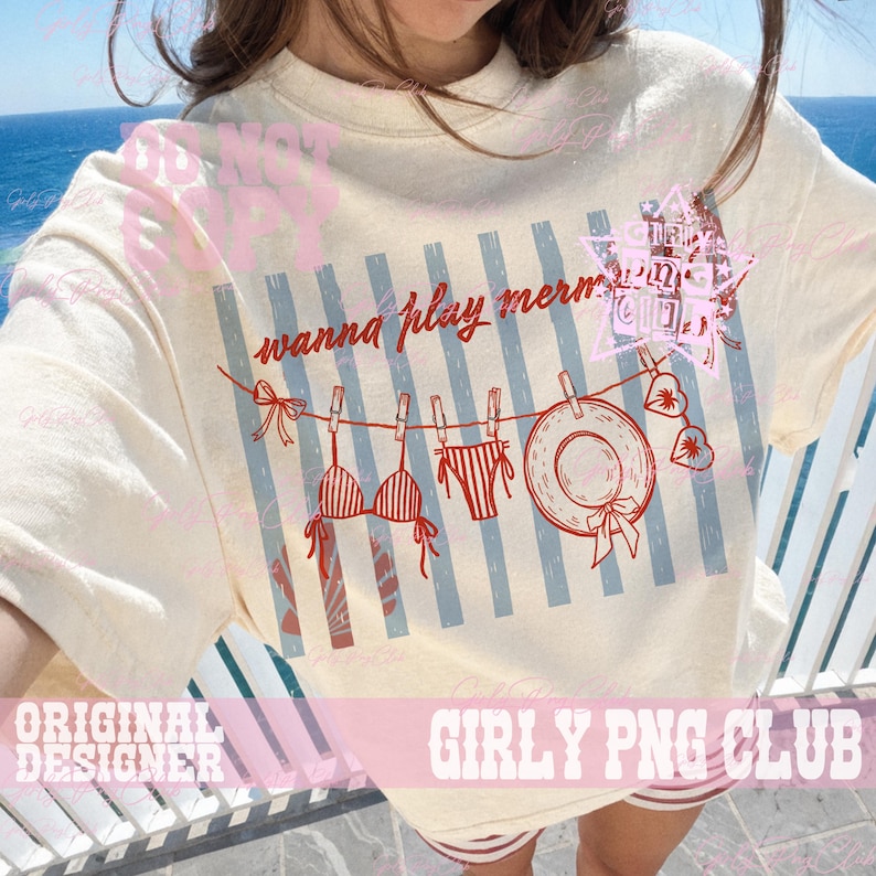 Op de afbeelding: Cr&egrave;mekleurig T-shirt met een strandthema. Het ontwerp omvat een waslijn met een bikini, zwembroek en zonnehoed. De tekst "wanna play merms" staat boven de waslijn.