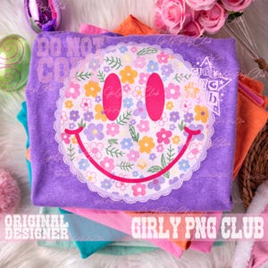May include: A stack of colorful t-shirts, with a purple shirt on top featuring a floral smiley face design. The smiley face has pink eyes and a red smile. The text "DO NOT COPY" is visible on the top shirt. The words "GIRLY PNG CLUB" are also visible.