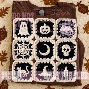 May include: A brown t-shirt featuring a grid of nine square crochet patches. Each patch has a black center with a white crocheted Halloween motif, including a ghost, pumpkin, bat, spiderweb, crescent moon, skull, cat, witch hat, and candle.