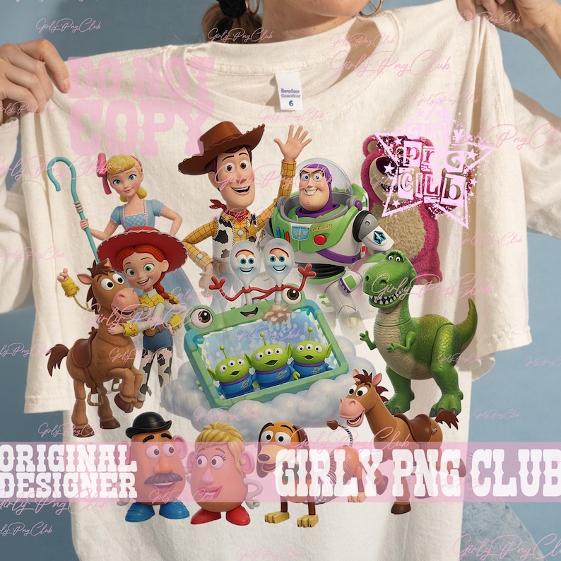 Puede incluir: Una camiseta de color crema con un estampado gr&aacute;fico de varios personajes de juguetes animados, incluyendo un vaquero, un guardi&aacute;n espacial, una vaquera, un caballo, un dinosaurio, figuras de patata y tres peque&ntilde;os alien&iacute;genas verdes en un marco azul.
