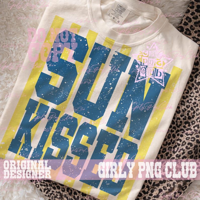 Pode incluir: Camiseta creme com as palavras "SUN KISSED" em letras azuis desgastadas, sobre listras verticais amarelas. A camiseta tamb&eacute;m apresenta o texto "ORIGINAL DESIGNER" e "GIRLY PNG CLUB".
