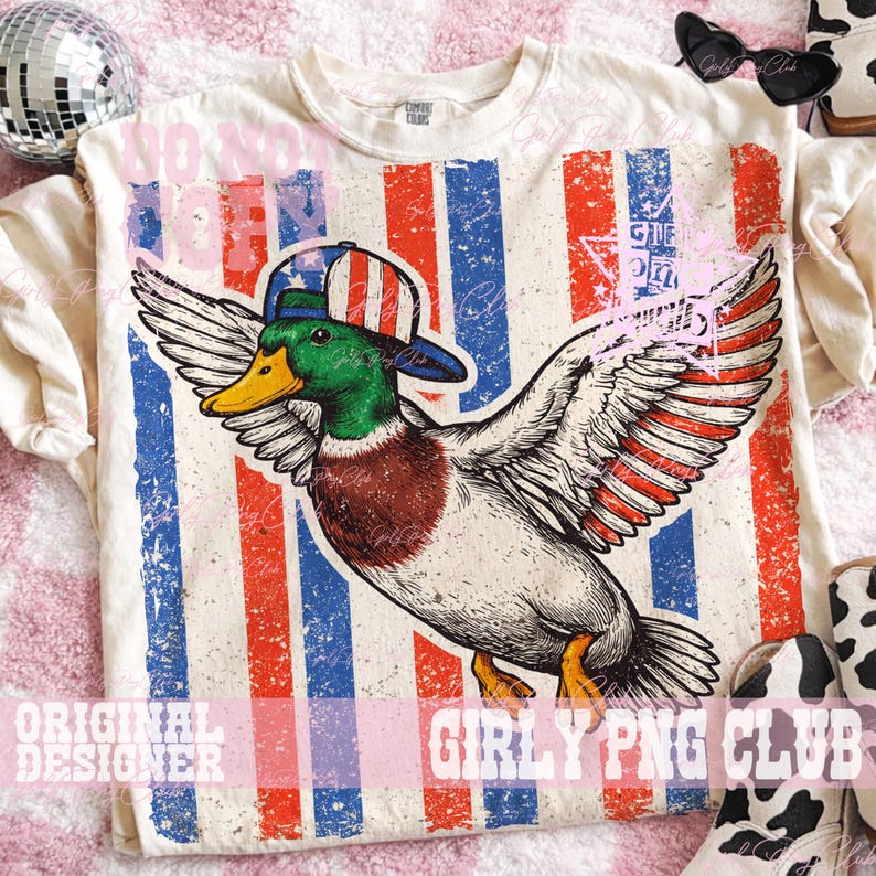 Pu&ograve; includere: T-shirt color crema con grafica di un'anatra con cappello patriottico, ali spiegate su sfondo a strisce rosse, bianche e blu. La maglietta ha il testo "Do Not Disturb" e "Original Designer".
