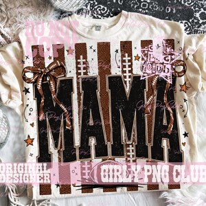 May include: A cream-colored t-shirt featuring a graphic print with the word MAMA in large black block letters. The design includes brown football-textured vertical stripes, white football laces, brown bows, and small orange stars.