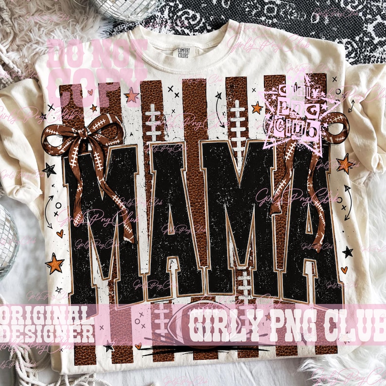 May include: A cream-colored t-shirt featuring a graphic print with the word MAMA in large black block letters. The design includes brown football-textured vertical stripes, white football laces, brown bows, and small orange stars.