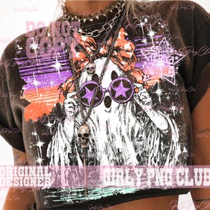 May include: A dark brown t-shirt featuring a graphic of a white ghost wearing a large orange bow and purple star-shaped sunglasses. The design includes a purple and orange sunset background with white stars and a star-shaped logo containing the text GIRLY PNG CLUB.