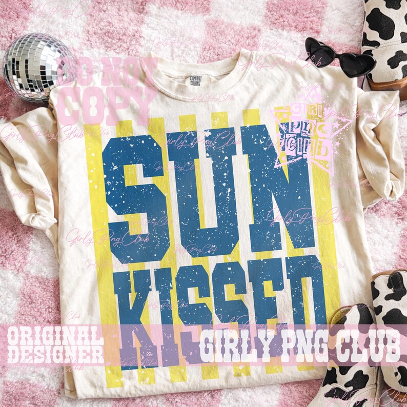 Pode incluir: Camiseta creme com as palavras "SUN KISSED" em letras azuis desgastadas. Listras verticais amarelas percorrem a camiseta. A camiseta &eacute; estilizada com &oacute;culos de sol, uma bola de discoteca e botas com estampa de vaca.