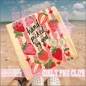 Puede incluir: Una toalla a rayas amarillas y rosas con fresas, corazones y margaritas. Se muestra el texto "hand picked by god", junto con la palabra "John" y el versículo 15:16. La toalla está en una playa de arena.