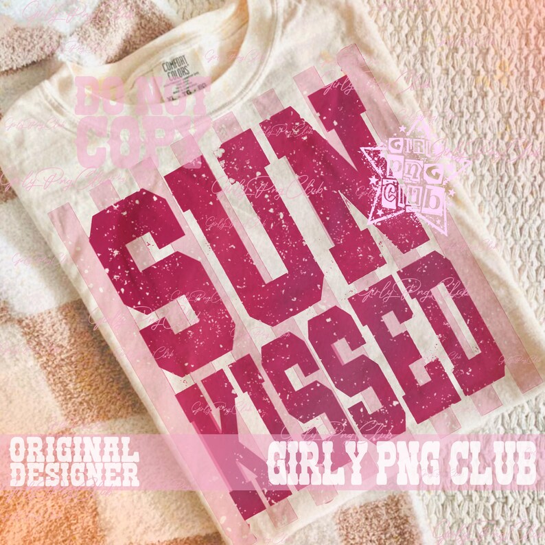Pode incluir: Camiseta creme com gola redonda com as palavras "SUN KISSED" em letras de bloco rosa escuro desgastadas. A camiseta tem um visual vintage desbotado, com listras rosa verticais atr&aacute;s do texto. A camiseta est&aacute; dobrada em uma superf&iacute;cie estampada.