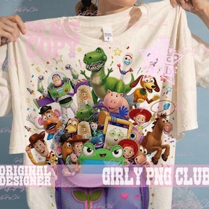 Puede incluir: Una camiseta de color crema con un estampado gr&aacute;fico colorido de varios personajes de juguetes animados, incluyendo un guardi&aacute;n espacial, un dinosaurio verde, un vaquero y una vaquera, saliendo de una mochila morada, con estrellas y confeti.