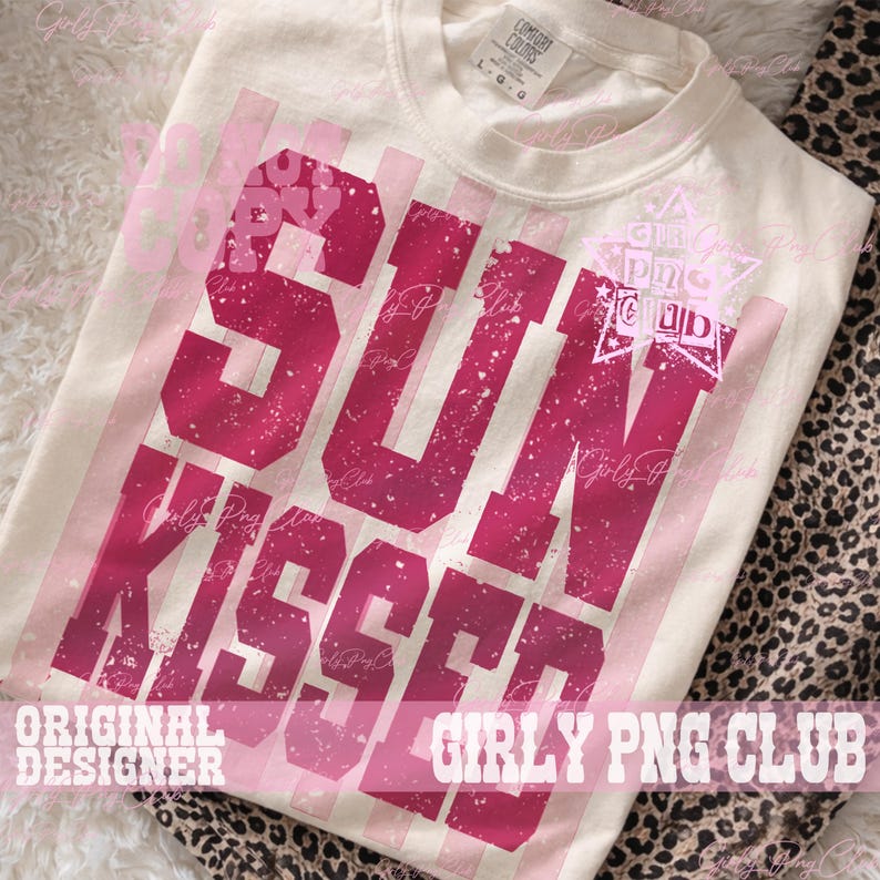 Pode incluir: Camiseta creme com as palavras "SUN KISSED" em letras rosa desbotadas. A camiseta tamb&eacute;m apresenta listras rosa verticais e o texto "ORIGINAL DESIGNER" e "GIRLY PNG CLUB". A camiseta &eacute; feita de um material macio.