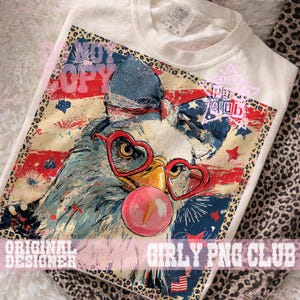 May include: Cream-colored t-shirt featuring a patriotic eagle design. The eagle wears heart-shaped glasses and a bow, blowing a bubblegum bubble. The design includes red, white, and blue elements, fireworks, and the text "Girly PNG Club."
