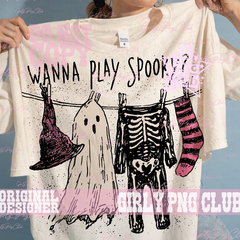 Op de afbeelding: Een off-white t-shirt met een zwarte afbeelding van een waslijn met een heksenhoed, een spook, een skeletkostuum en een gestreepte sok. De tekst "WANNA PLAY SPOOKY?" staat in het zwart boven de waslijn gedrukt met zwarte spikkels.