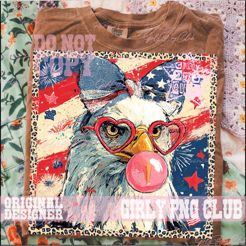 May include: Brown t-shirt featuring a graphic of an eagle wearing heart-shaped glasses and blowing a bubblegum bubble. The eagle is set against a backdrop of the American flag and fireworks. The text "Girly PNG Club" is visible.