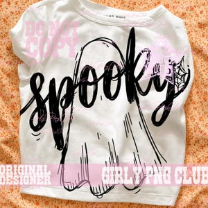Puede incluir: Una camiseta blanca con una ilustraci&oacute;n gr&aacute;fica negra de un fantasma y la palabra SPOOKY escrita en una fuente cursiva estilizada en el centro. El dise&ntilde;o incluye un peque&ntilde;o detalle de telara&ntilde;a en el lado derecho del fantasma.