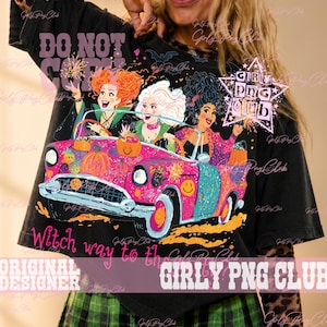 May include: A black t-shirt featuring a graphic of three cartoon witches with orange, white, and black hair riding in a bright pink and teal vintage convertible car. The design includes pumpkins, stars, and the text Witch way to the candy.