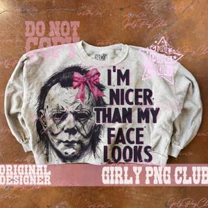 May include: A heather gray crewneck sweatshirt featuring a graphic of a horror movie character wearing a pink bow. The text reads I'M NICER THAN MY FACE LOOKS in bold black lettering. The garment has long sleeves and a ribbed collar and cuffs.