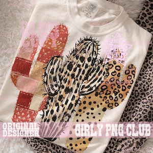May include: Cream-colored t-shirt featuring a colorful cactus design. The cactus has a patchwork design with shades of red, pink, and tan, and a leopard print pattern. The text "GIRLY PNG CLUB" is printed at the bottom.