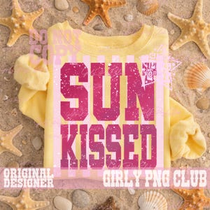 Pode incluir: Uma camisola amarela com as palavras "SUN KISSED" em letras rosa desgastadas. A camisa tem gola redonda e mangas compridas. O fundo inclui estrelas do mar, conchas e areia.