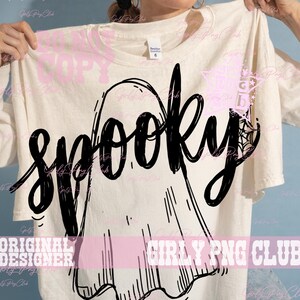 Puede incluir: Una camiseta de color crema con un gran gr&aacute;fico negro de un fantasma y la palabra "spooky" escrita en un estilo de letra cursiva y negrita en el centro. El dise&ntilde;o incluye un peque&ntilde;o detalle de telara&ntilde;a integrado en la letra y.