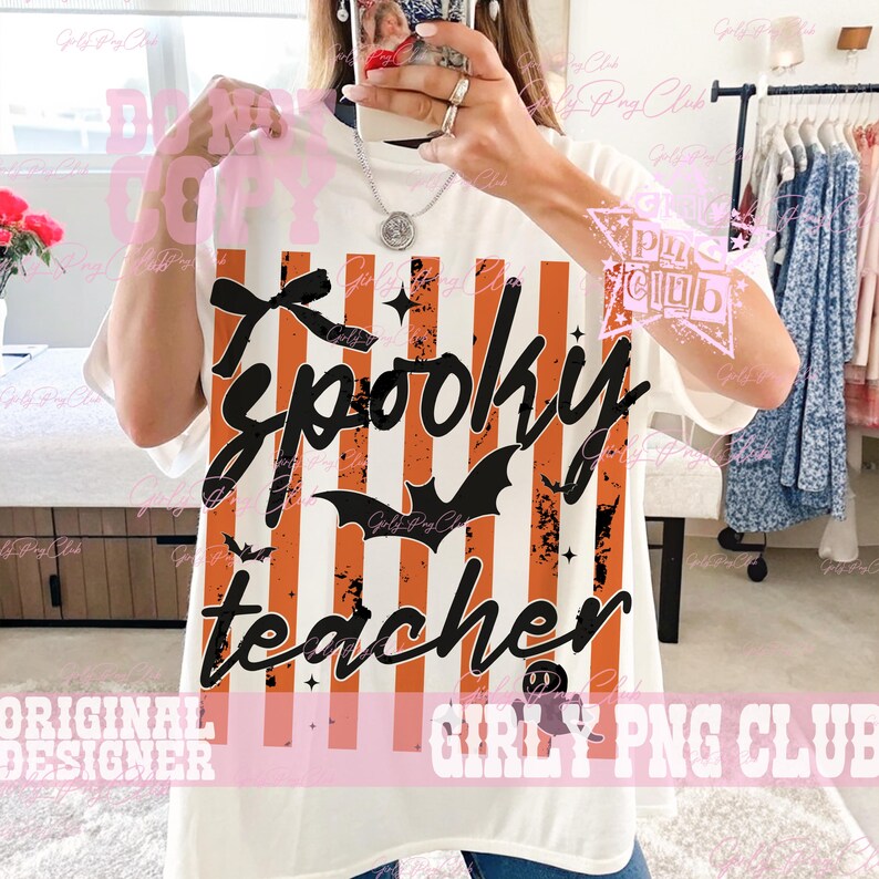 May include: A white short-sleeved t-shirt featuring a graphic print of vertical orange and black distressed stripes. The design includes the black cursive text Spooky teacher, a black bow, a black bat silhouette, and a small ghost icon.