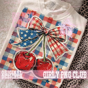 Puede incluir: Camiseta color crema con un diseño patriótico. El gráfico incluye un lazo a cuadros rojo y blanco, un lazo azul con estrellas blancas y dos cerezas rojas. Las palabras "Original Designer" y "Girly PNG Club" están impresas en la camiseta.