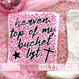 Peut inclure: T-shirt blanc avec un fond rose &agrave; imprim&eacute; l&eacute;opard et les mots "heaven top of my bucket list" en &eacute;criture noire. Une &eacute;toile noire et une croix sont &eacute;galement pr&eacute;sentes. Une botte blanche est visible &agrave; droite.