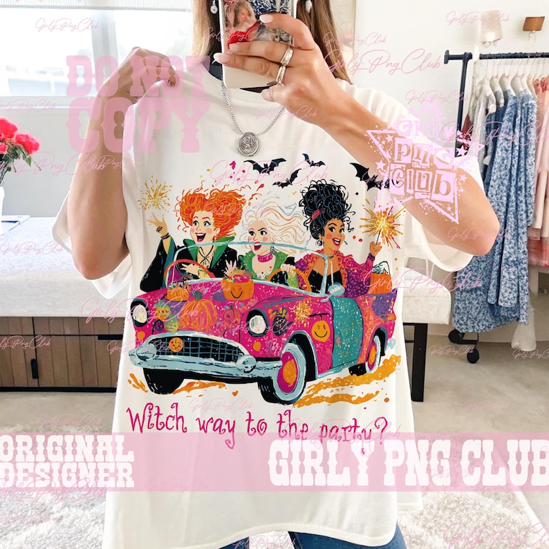 May include: A white t-shirt featuring a graphic of three women with distinct hairstyles riding in a bright pink convertible car. The design includes pumpkins, bats, and fireworks. The text "Witch way to the party?" is printed in pink below the car.